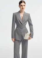 Medium shot of a woman in the belted grey blazer, holding a structured cream-colored clutch.