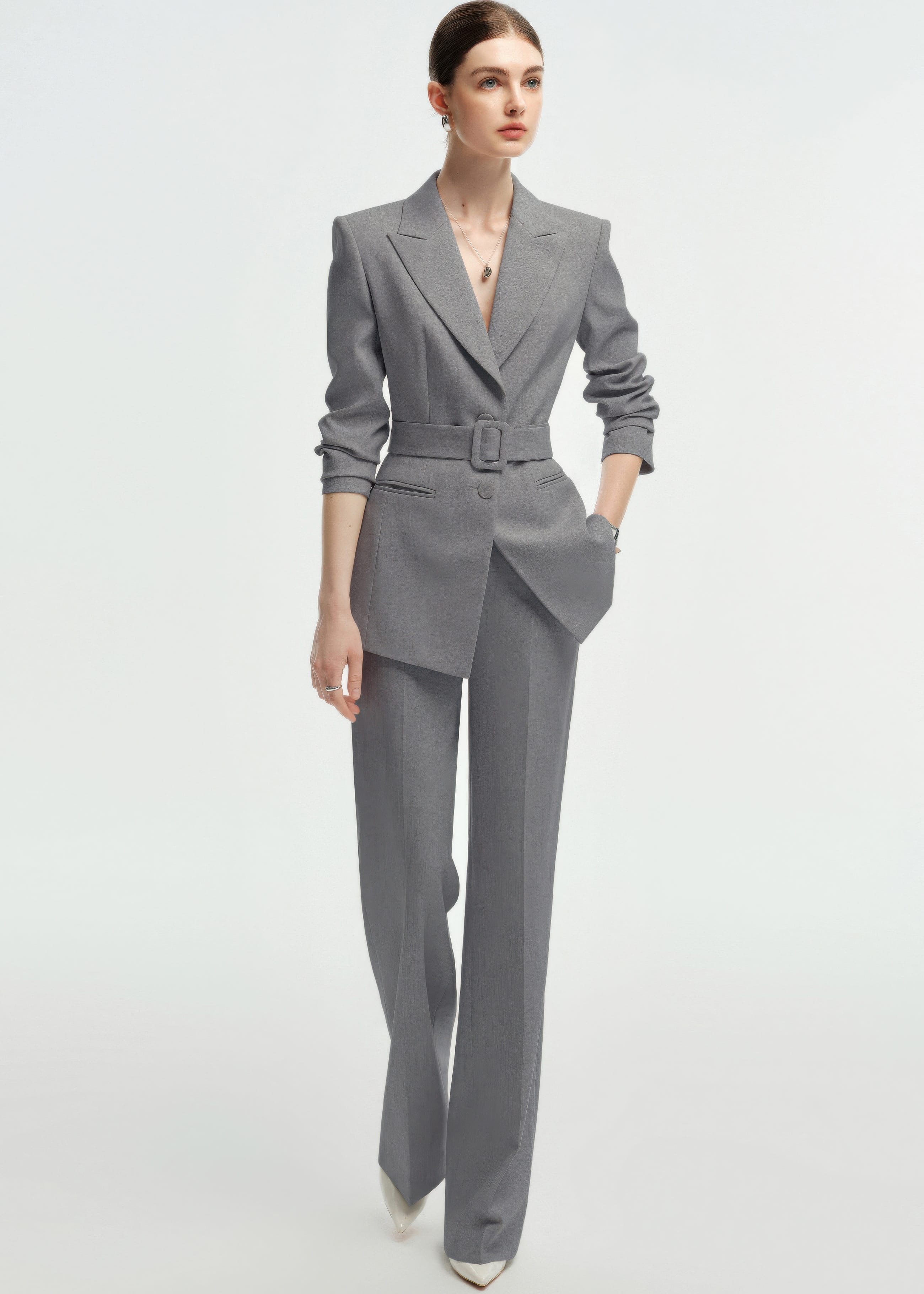 A full-body shot of the woman walking forward in the grey business suit and white heels.