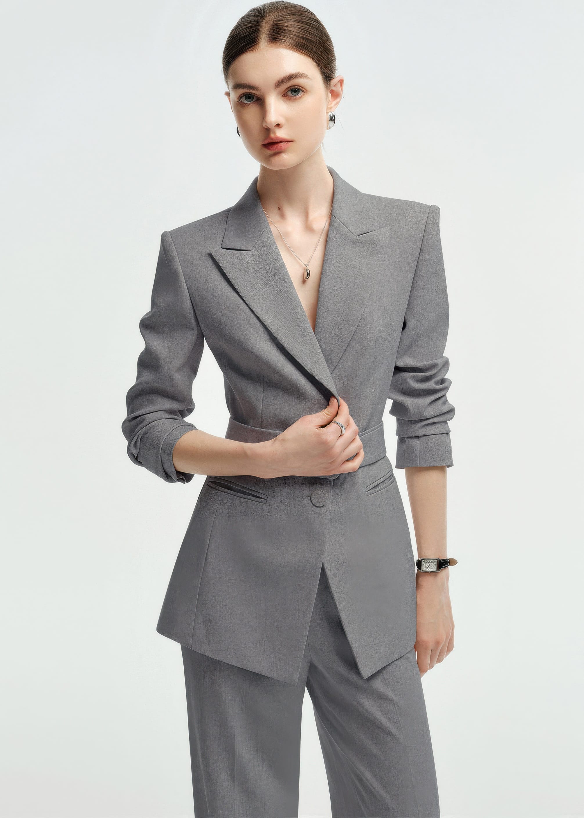 A waist-up shot of the woman adjusting the lapel of her grey belted blazer.