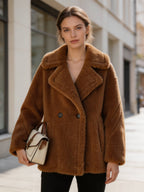 Model wearing a cognac brown shearling wool pea coat holding a small cream and brown structured handbag