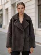 Front view of a model wearing a charcoal grey double-breasted shearling wool pea coat outdoors