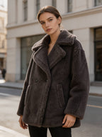 Three-quarter view of a model wearing an oversized dark grey shearling wool double-breasted pea coat