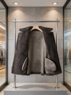 Inside lining and interior pockets view of an open charcoal grey shearling wool coat on a display rack