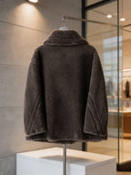  Back view of a dark grey shearling wool double-breasted pea coat displayed on a stand in a boutique