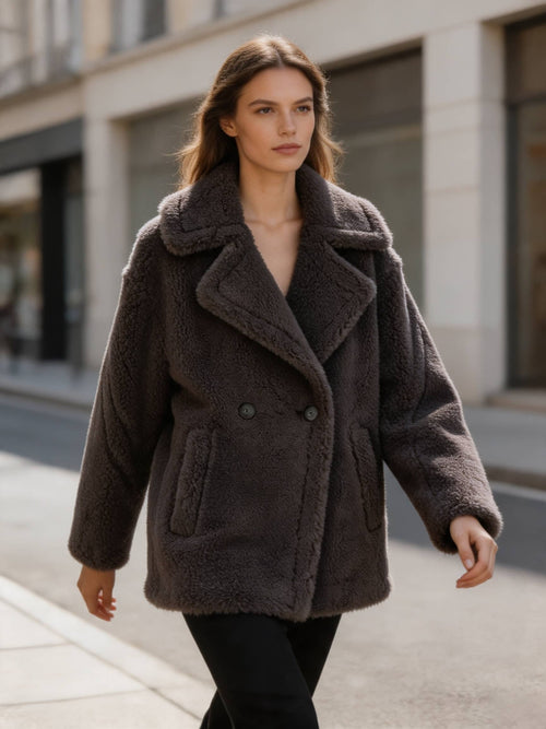 Model walking on a street wearing a dark grey double-breasted shearling wool pea coat with wide lapels