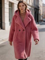Full-length street style view of a woman walking in a fuchsia pink hooded double-breasted genuine shearling coat.