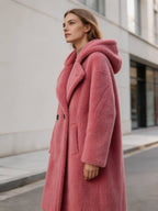 Three-quarter side angle showing the plush texture and side pocket of a women's fuchsia pink hooded shearling fur coat.