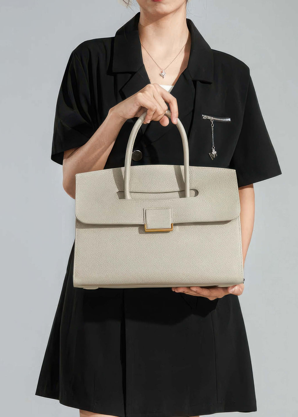 A front-facing lifestyle shot of a woman holding the handbag by its top handles, providing a clear perspective of the bag's proportions relative to the body.