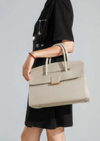 A side-profile lifestyle shot of a woman wearing a black dress, carrying the cream leather tote over her arm to demonstrate its size and how it hangs.