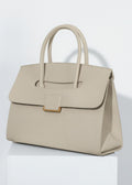 A professional studio shot of the genuine leather tote sitting on a white pedestal. The lighting highlights the fine pebbled texture of the leather and the gold-tone hardware.
