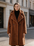 Model wearing a brown long hooded shearling wool teddy coat standing outdoors on a city street