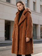 Three-quarter front view of a model in a brown oversized long hooded shearling wool teddy coat