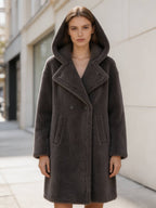 Front view of a model in a dark grey double-breasted hooded shearling teddy coat with hood up