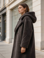 Side profile view of a model wearing a dark grey hooded shearling wool teddy coat