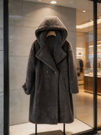 Front view of a dark grey double-breasted long hooded shearling coat displayed on a hanger in a boutique showcase