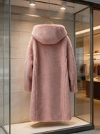 Back view display of a women's dusty pink hooded shearling long teddy coat hanging in a boutique window showcase.
