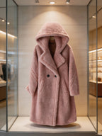 Front view product display of a women's dusty pink hooded double-breasted shearling long coat styled over a turtleneck sweater.