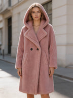 Front view portrait of a woman wearing a dusty pink hooded double-breasted plush shearling wool long coat.