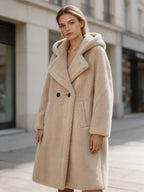 Medium shot of a model wearing a beige hooded double-breasted wool shearling coat with wide lapels and front pockets.