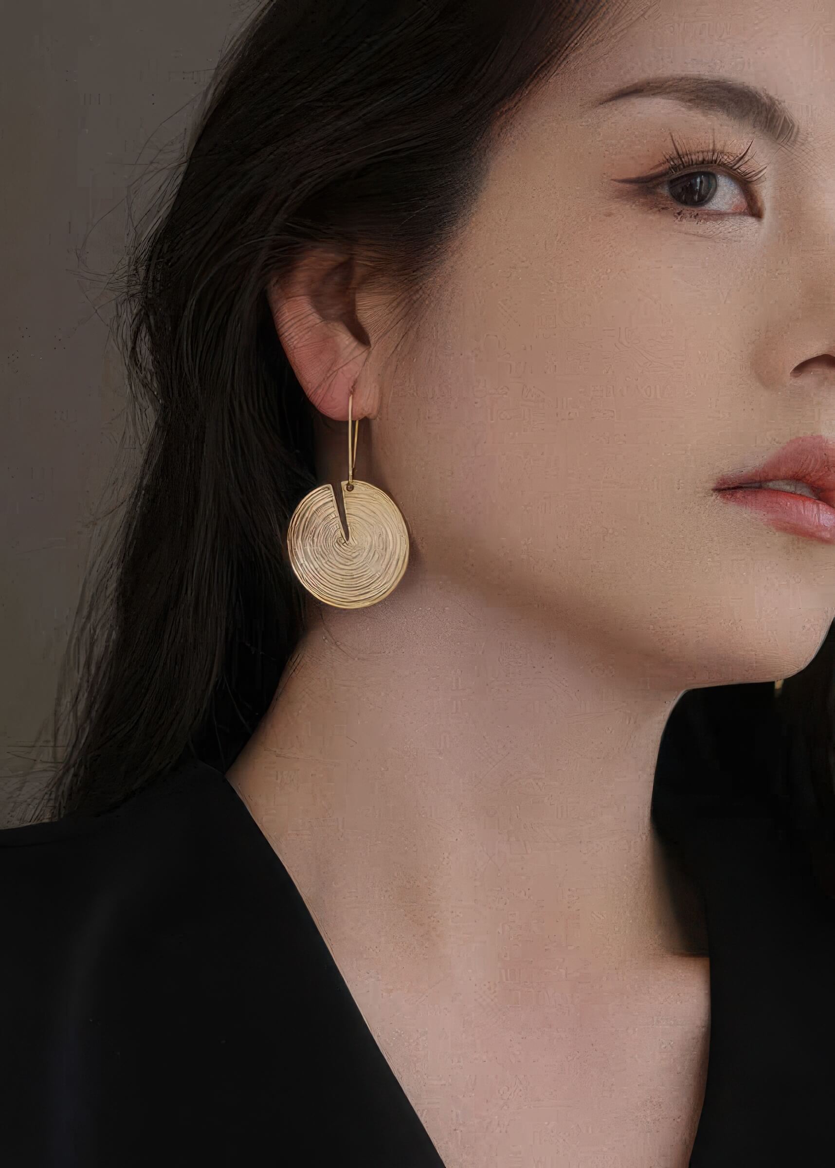 Close-up side view of a gold circular drop earring featuring a unique vertical slit design and a thin wire hook.