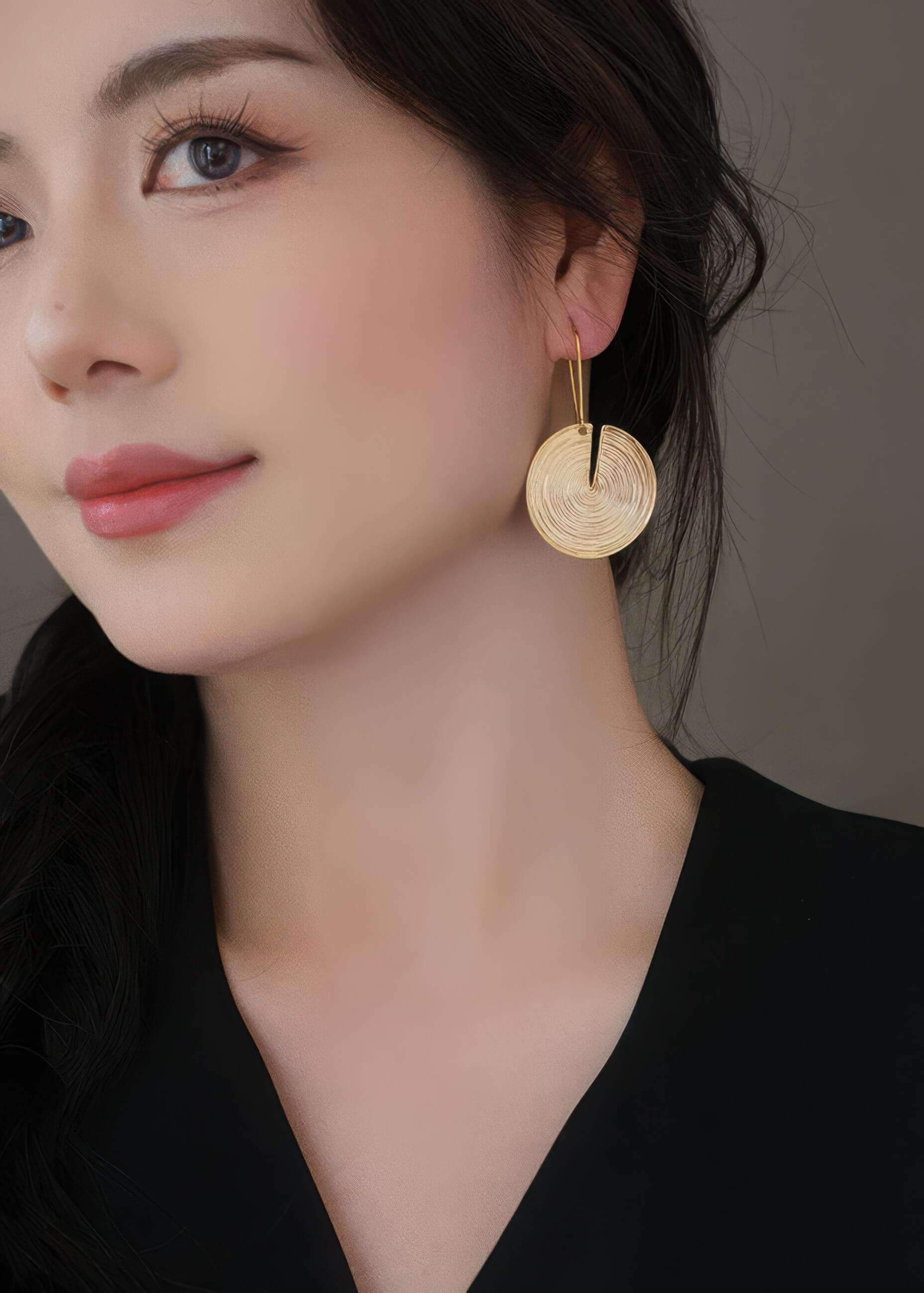 Close-up of a gold metal drop earring on a model, highlighting the textured spiral pattern and elegant long hook.