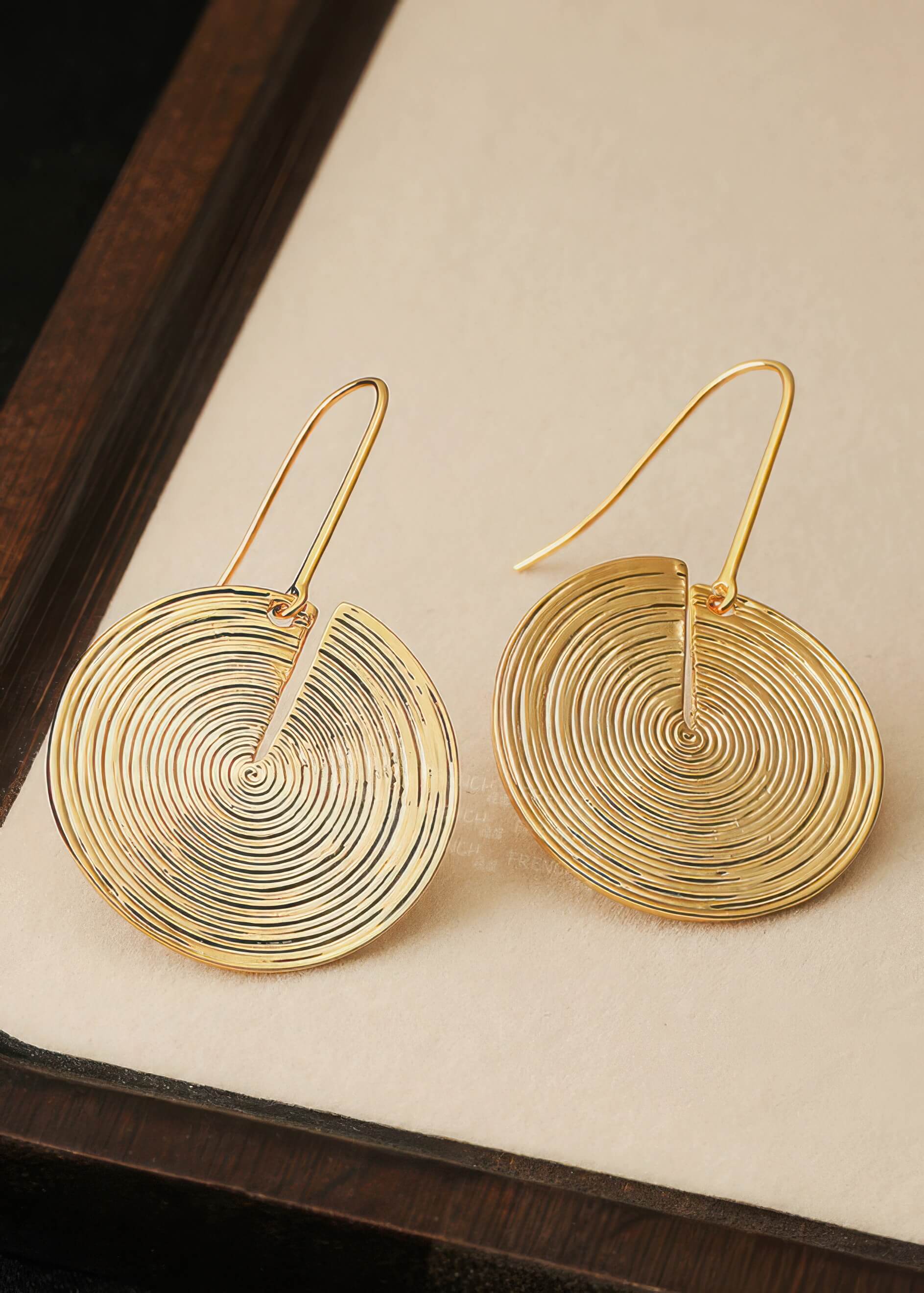 Detailed top-down shot of two gold textured disc earrings showing the delicate spiral ridges and thin ear wires.