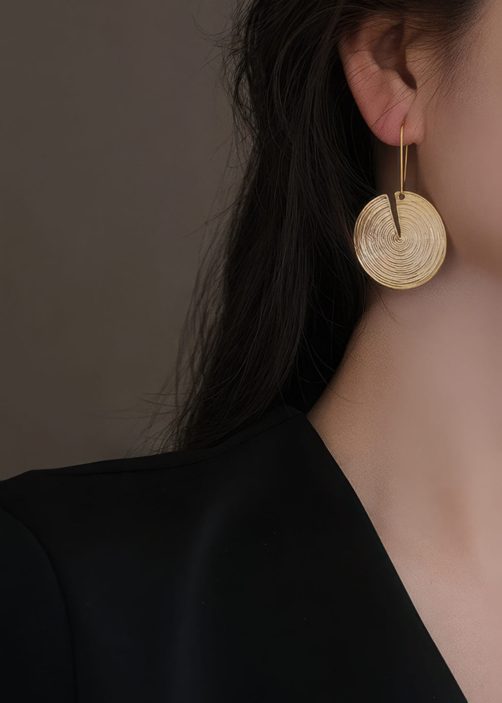 Profile view of a model wearing a large gold-plated circular drop earring with a minimalist modern aesthetic.