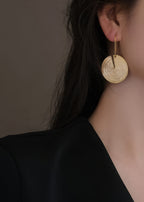 Profile view of a model wearing a large gold-plated circular drop earring with a minimalist modern aesthetic.