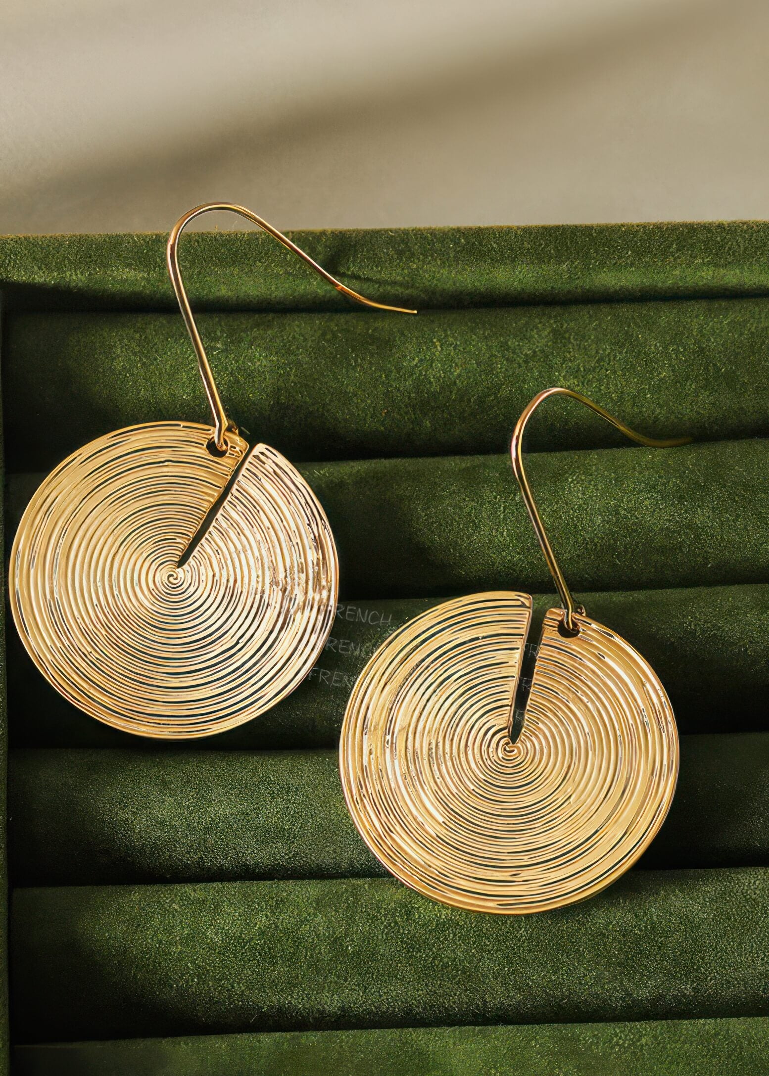 Pair of gold-toned disc earrings with a fine ripple texture displayed inside a dark green velvet jewelry box.