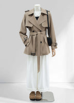 A full-length front view of the outfit. The khaki trench coat is paired with wide-leg white trousers and tan suede clogs, presenting a complete chic, professional look.