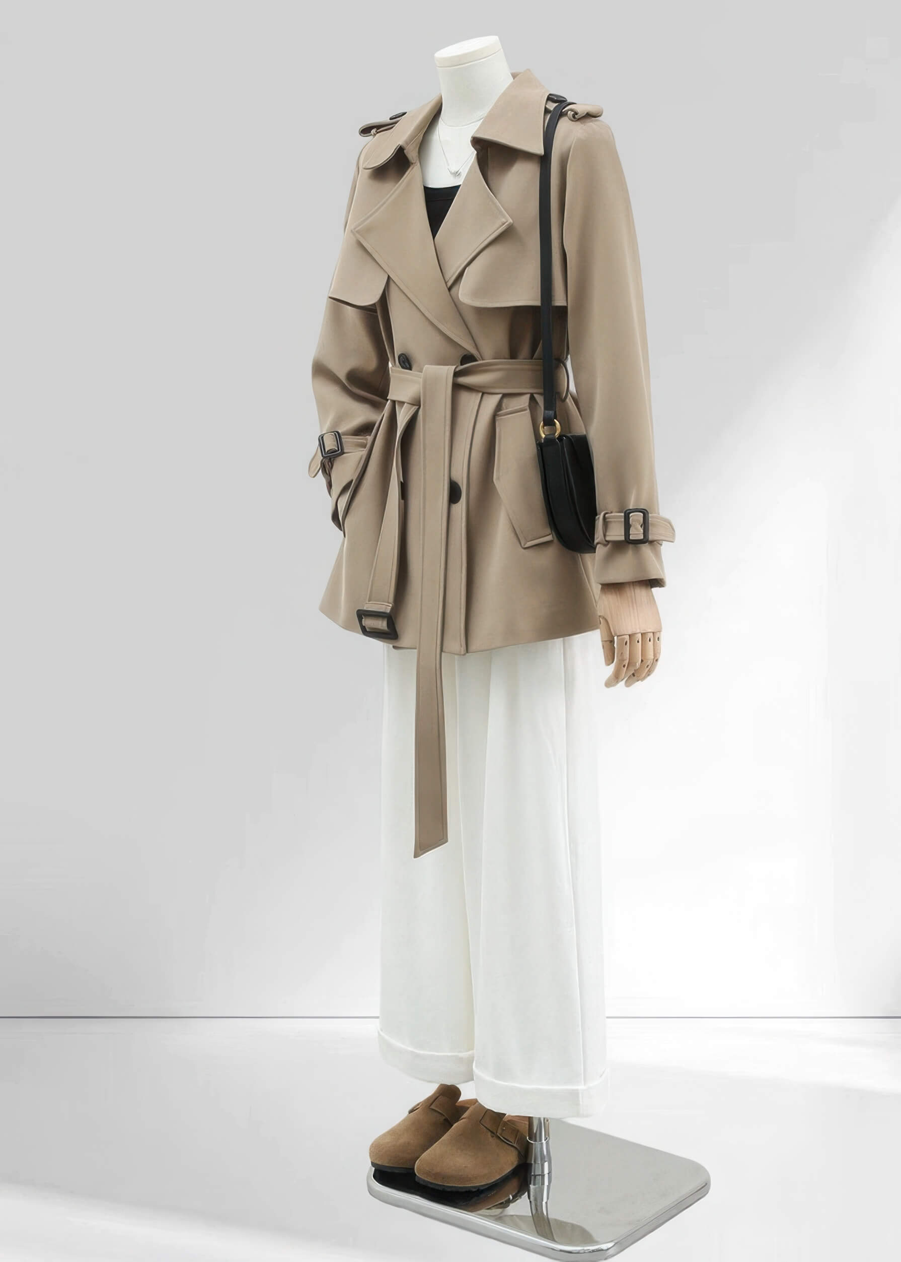 A full-length perspective shot from a slight angle. The mannequin is styled with a small black crossbody bag, showcasing how the short trench coat pairs with modern accessories and casual footwear.