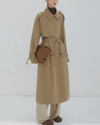 Front view of a women's long khaki double-breasted trench coat with waist belt and oversized fit.