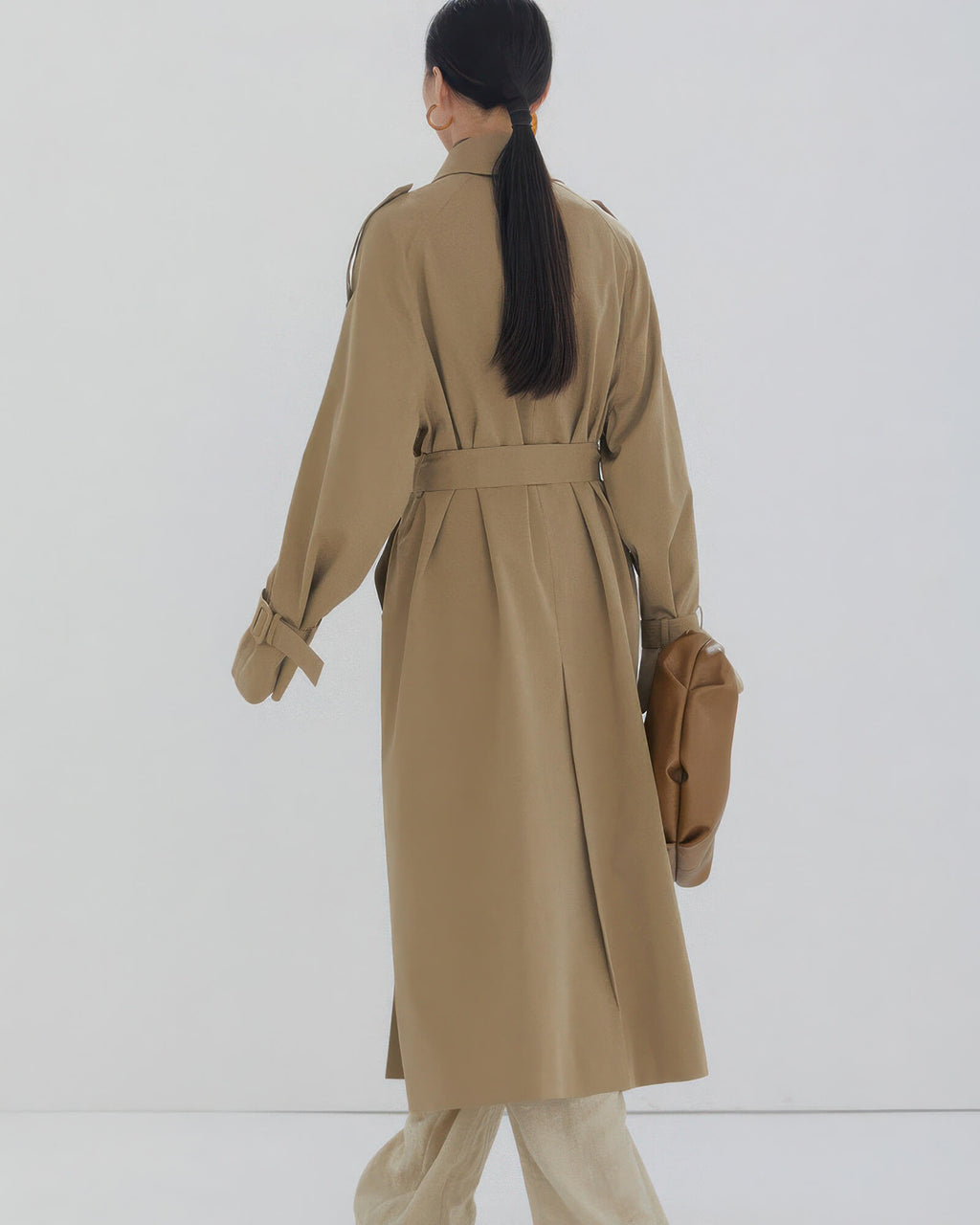Back view of a women's long oversized trench coat showing classic storm flap and center vent detail.