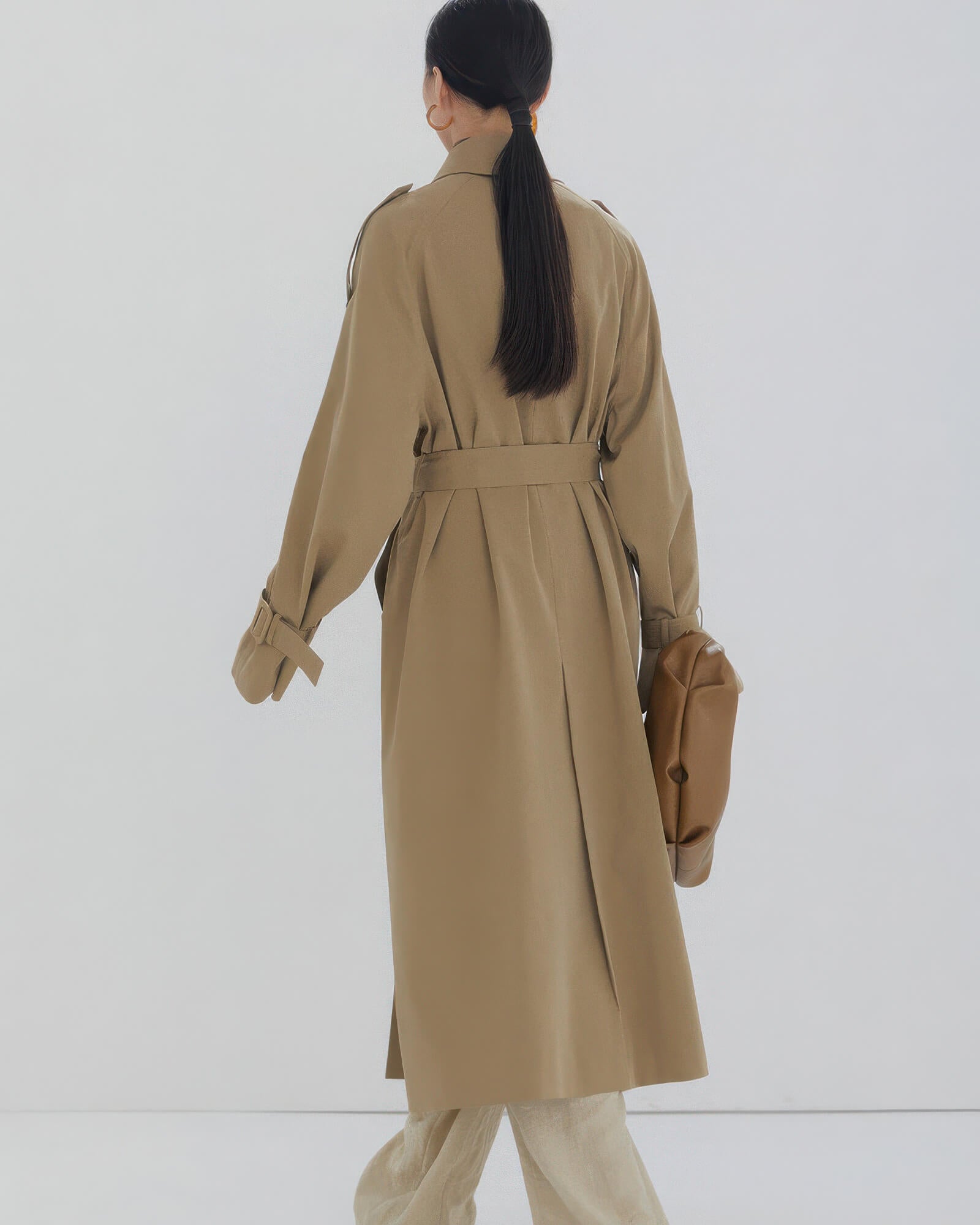 Back view of a women's long oversized trench coat showing classic storm flap and center vent detail.