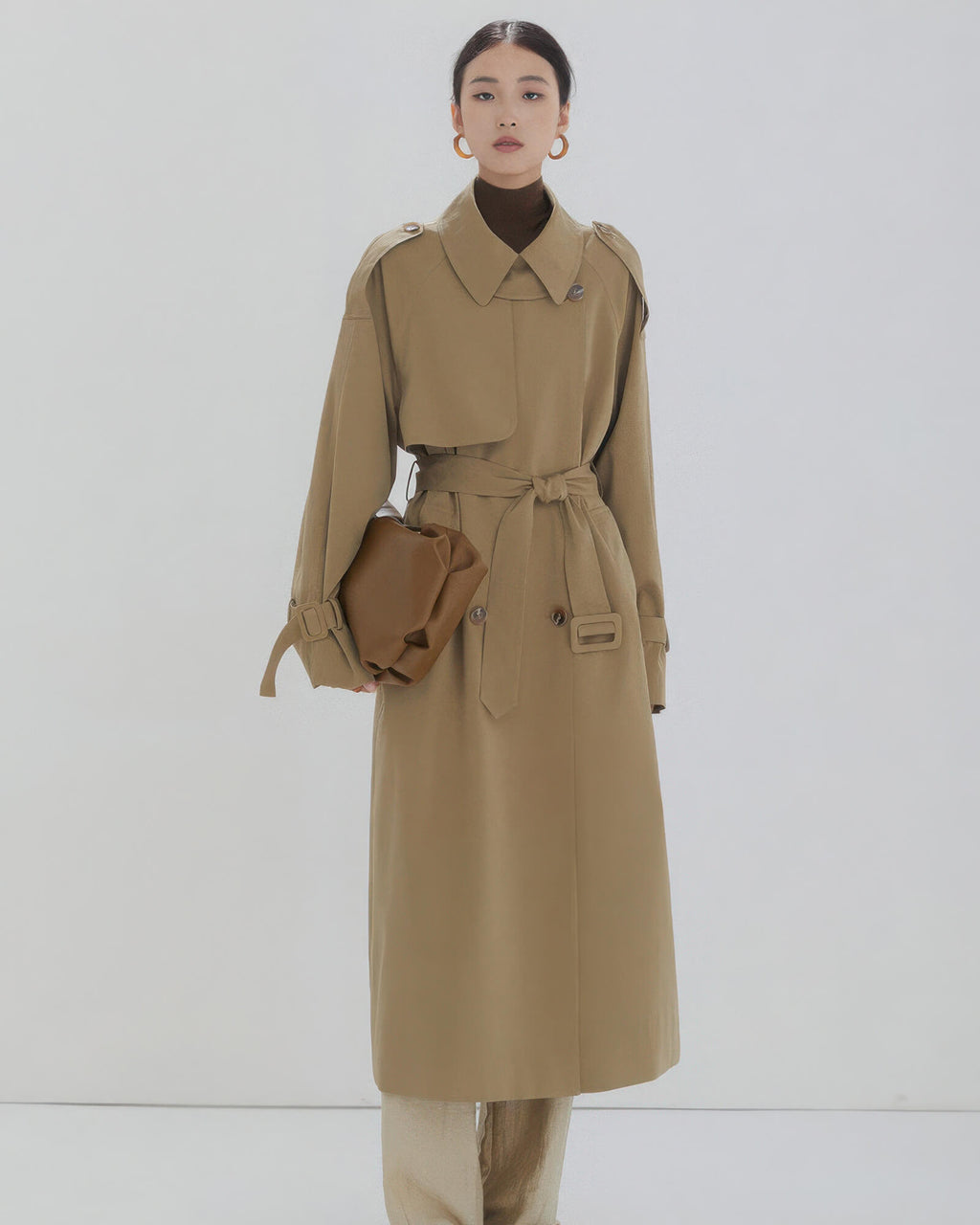 Full-length view of women's long khaki double-breasted trench coat with tied waist belt and relaxed fit.