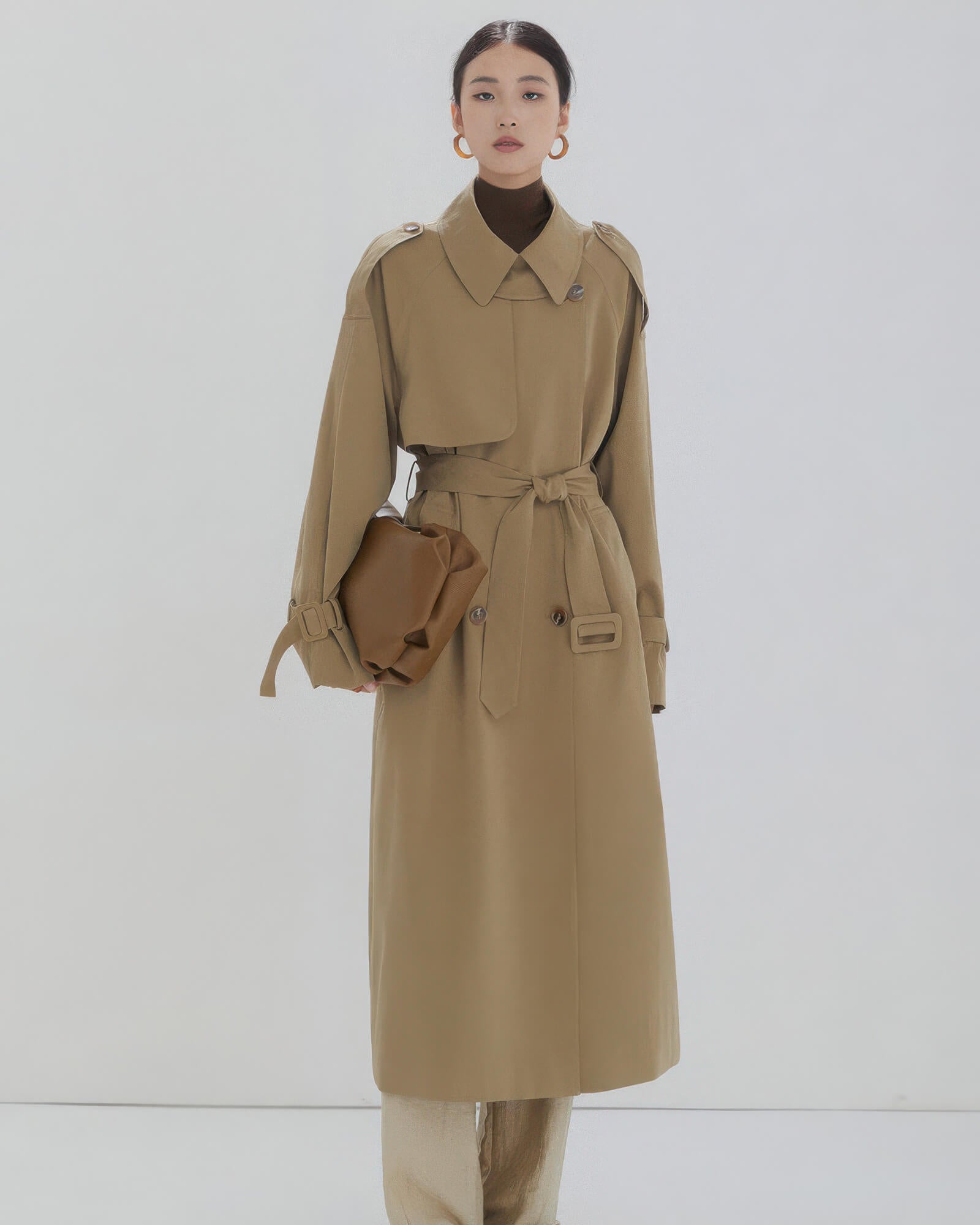 Full-length view of women's long khaki double-breasted trench coat with tied waist belt and relaxed fit.