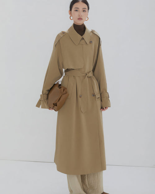 Front view of a women's long khaki double-breasted trench coat with waist belt and oversized fit.