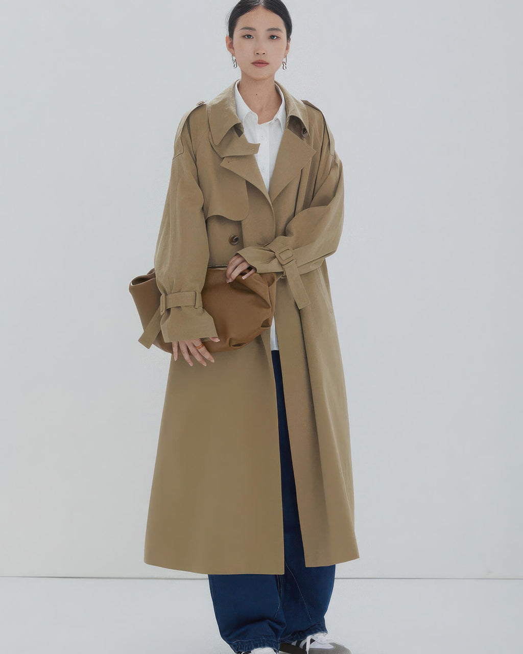 Minimalist women's camel trench coat worn open with white shirt and wide-leg denim jeans.
