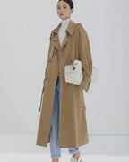 Long beige double-breasted trench coat for women styled with light blue jeans and white turtleneck.