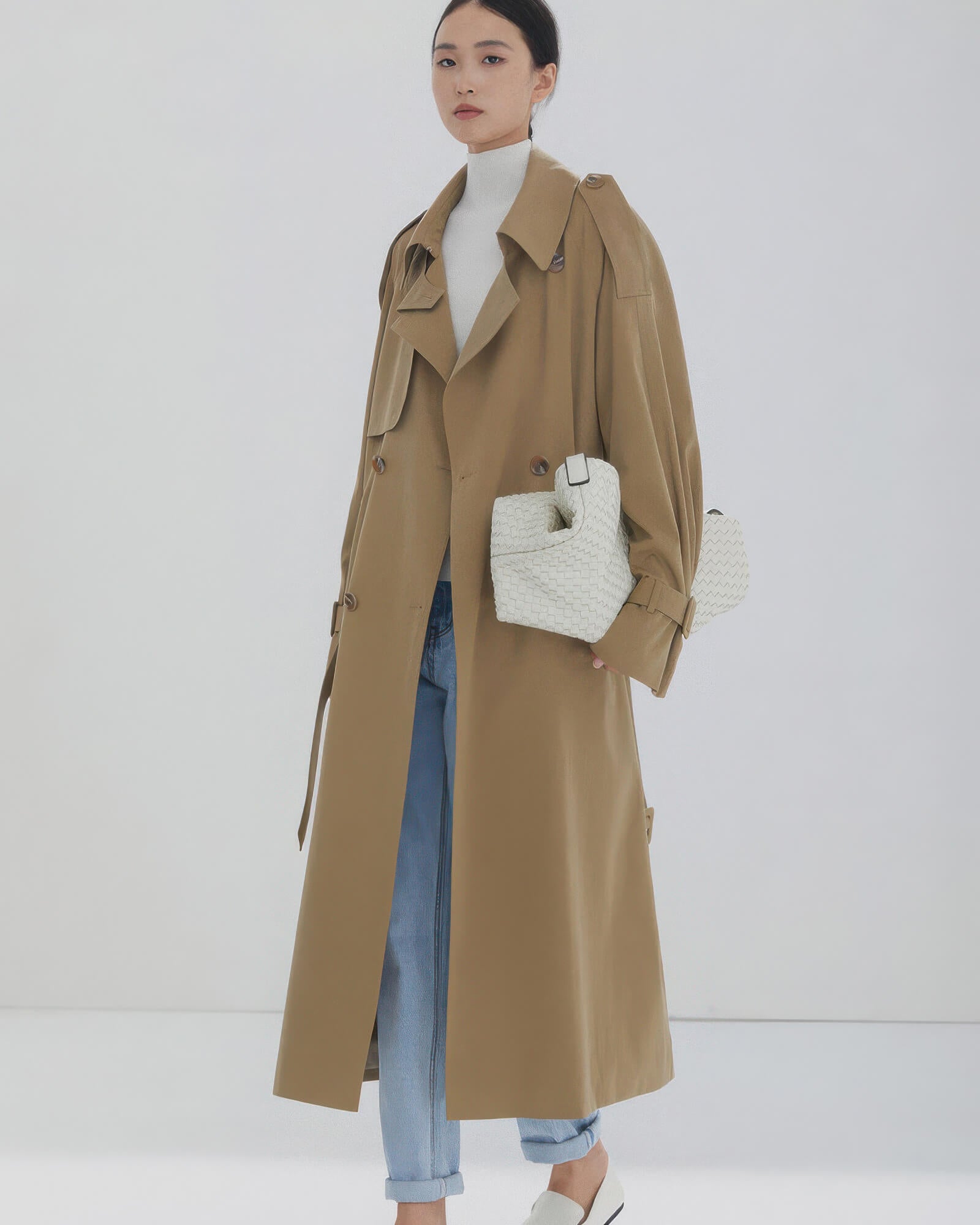 Long beige double-breasted trench coat for women styled with light blue jeans and white turtleneck.