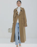 Long beige double-breasted trench coat for women styled with light blue jeans and white turtleneck.