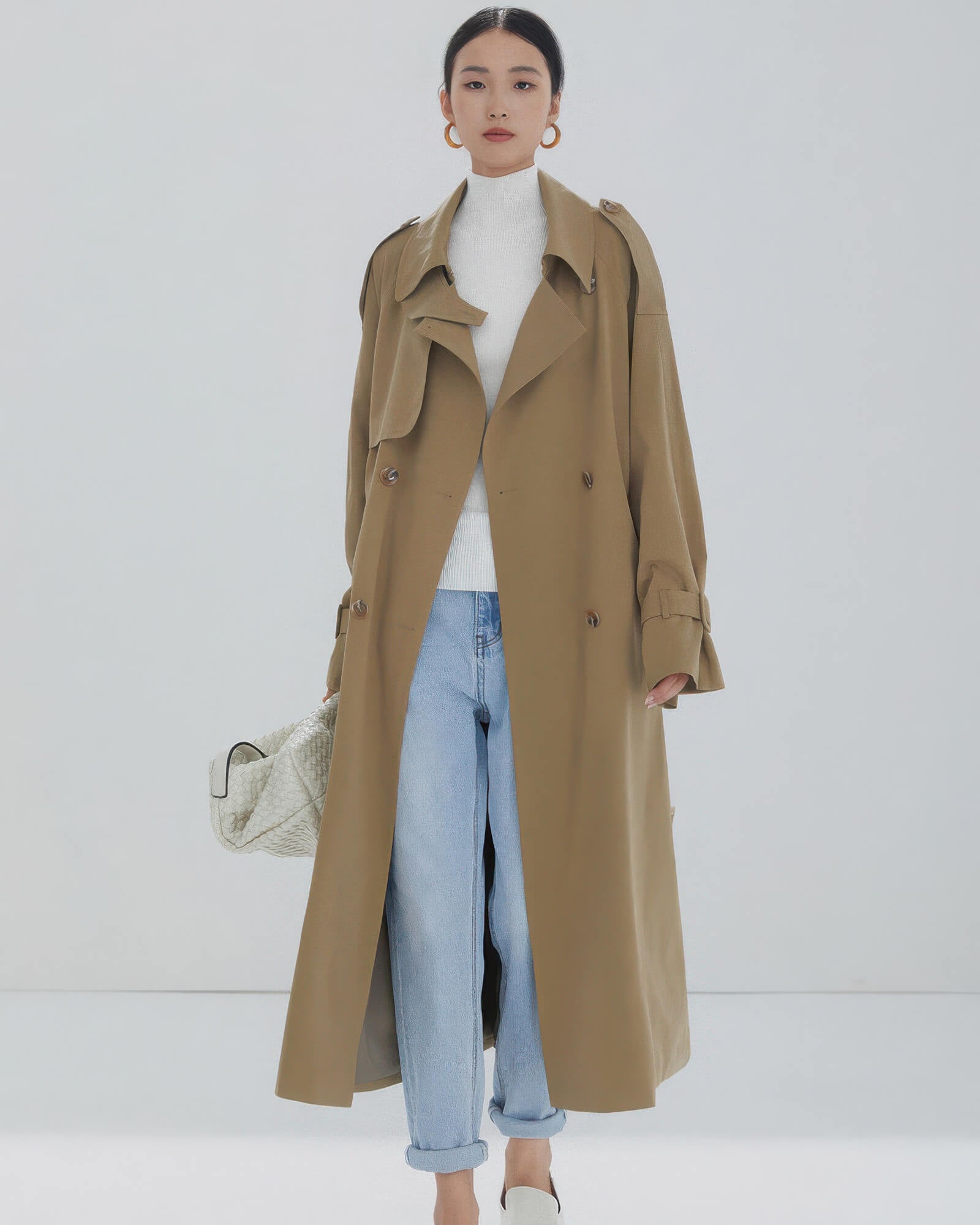 Long beige double-breasted trench coat for women styled with light blue jeans and white turtleneck.