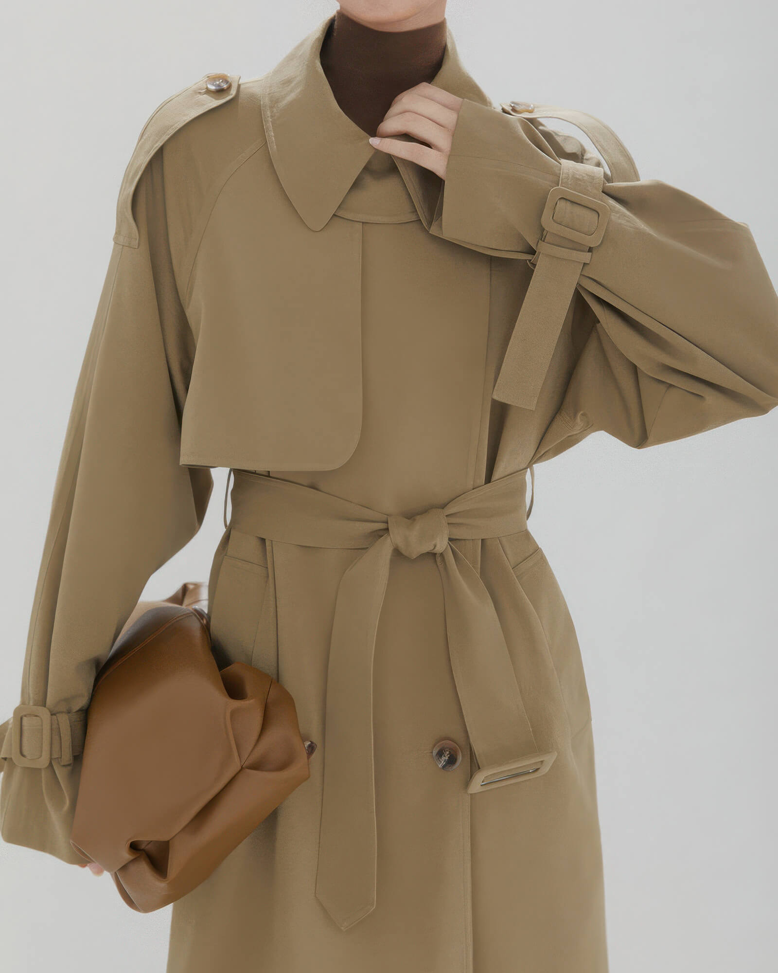 Close-up detail of double-breasted buttons and adjustable waist belt on a classic khaki trench coat.