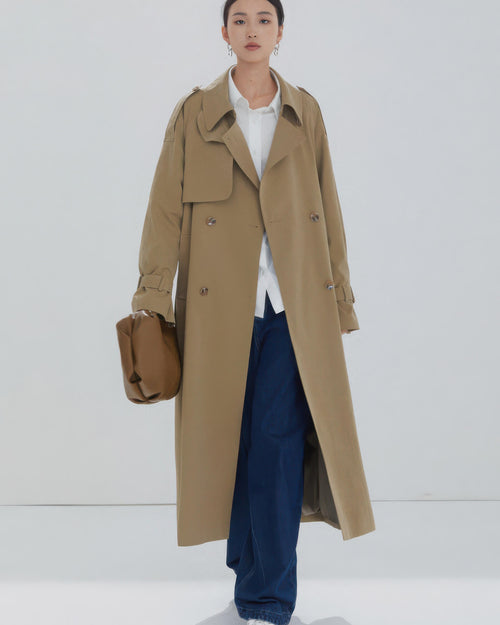 Minimalist women's camel trench coat worn open with white shirt and wide-leg denim jeans.