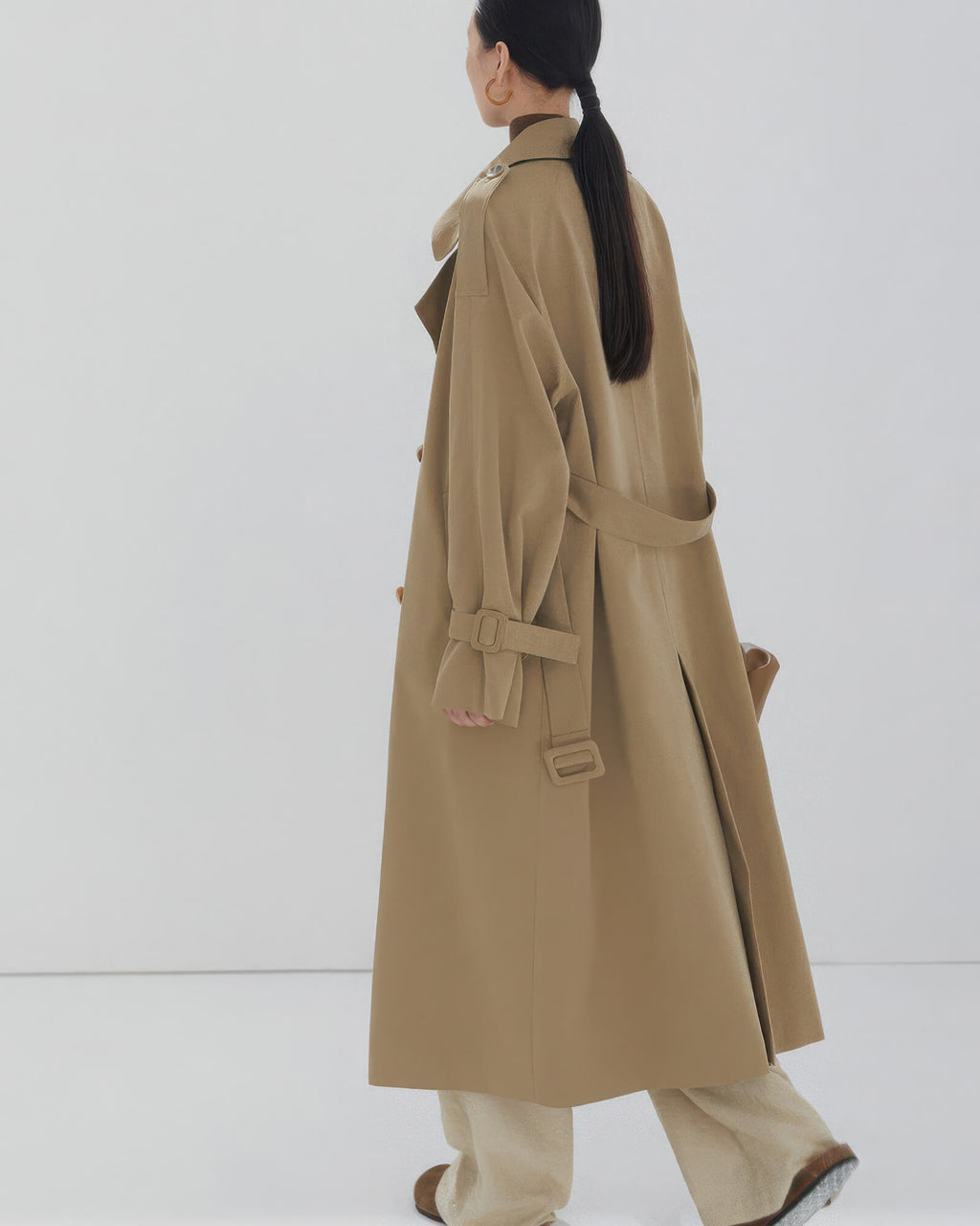 Back view of a women's long oversized trench coat showing classic storm flap and center vent detail.