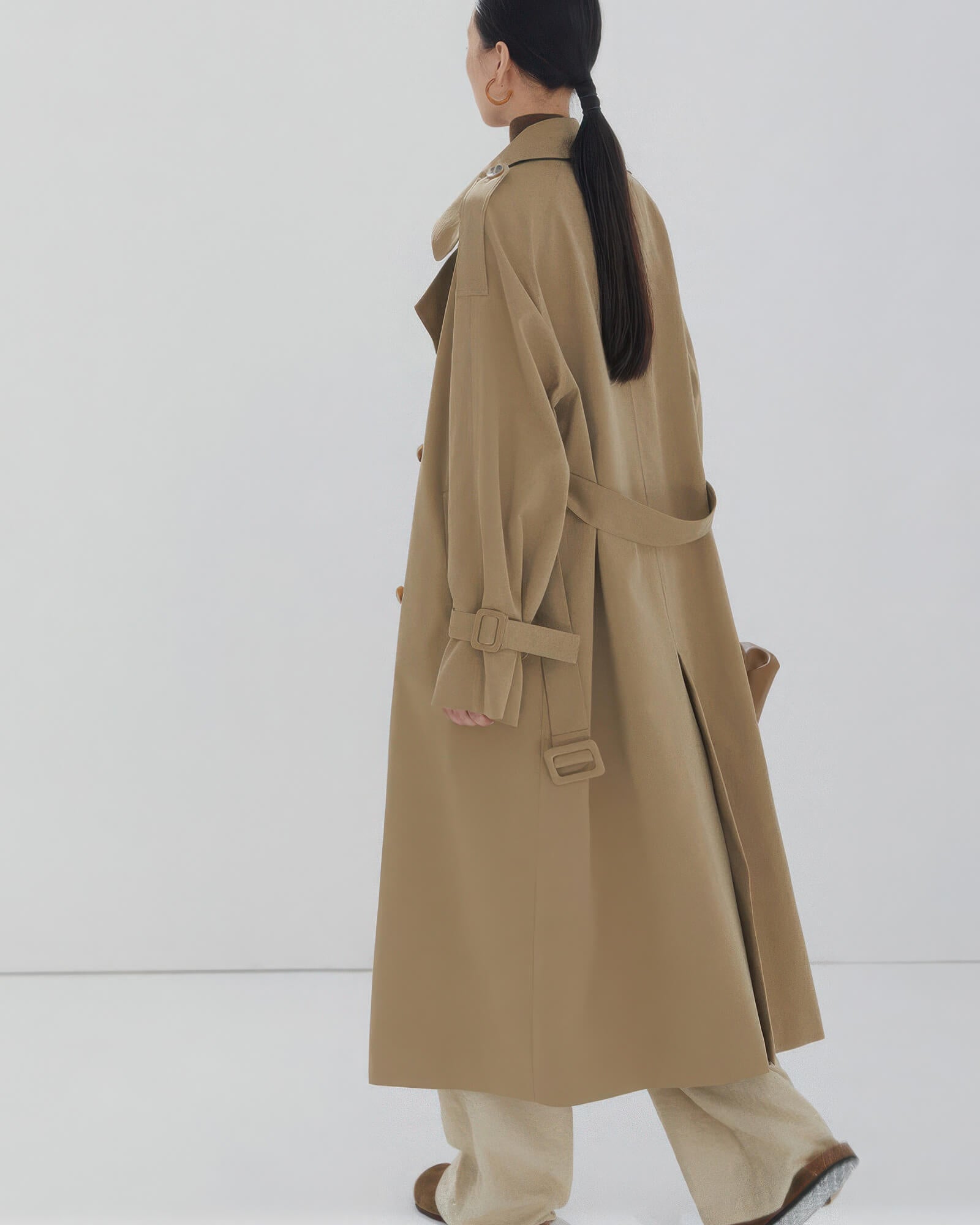 Back view of a women's long oversized trench coat showing classic storm flap and center vent detail.