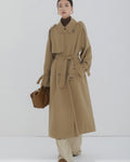 Front view of a women's long khaki double-breasted trench coat with waist belt and oversized fit.