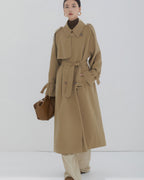 Front view of a women's long khaki double-breasted trench coat with waist belt and oversized fit.