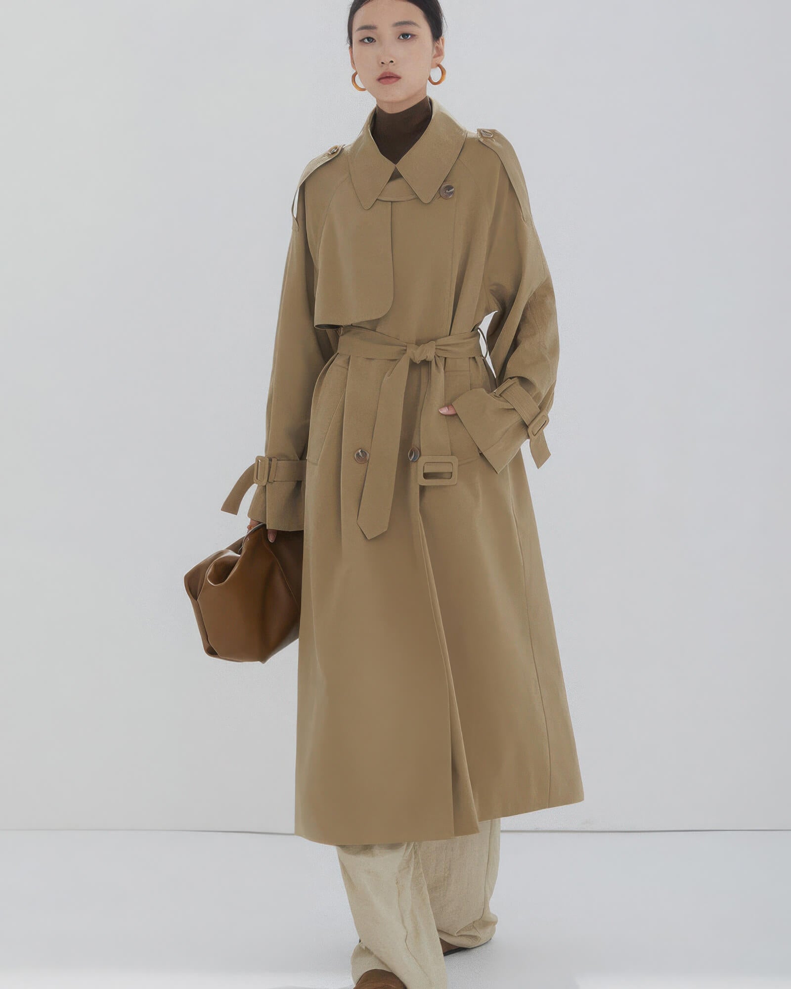 Front view of a women's long khaki double-breasted trench coat with waist belt and oversized fit.