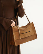 Side view of the minimalist suede shoulder bag in brown, highlighting the textured material, top zipper, and decorative side stitching.